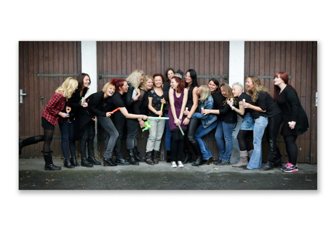 Viele junge Frauen stehen vor eine Holztor und lachen Fotoparty JGA Fotoshooting Dortmund